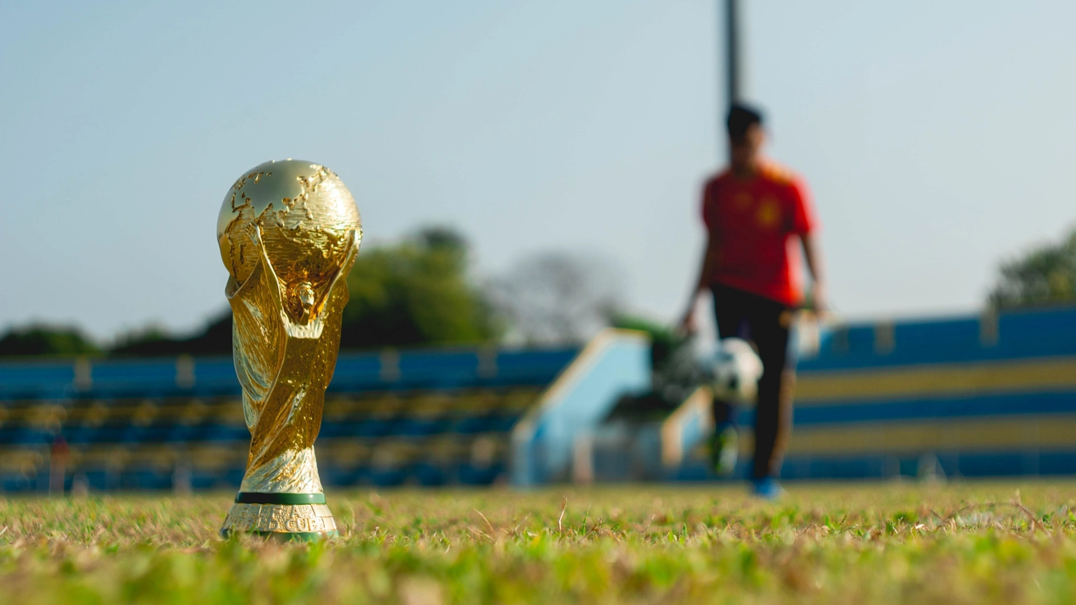 Photo of world cup in foreground and footballer out of focus in the background