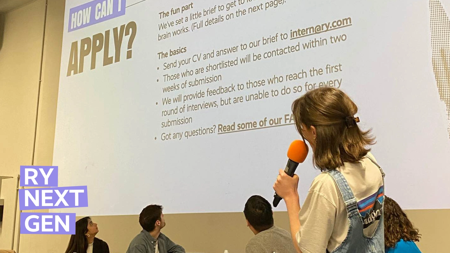 Annie Counsell holding a microphone, presenting information about RY's Next Gen internship