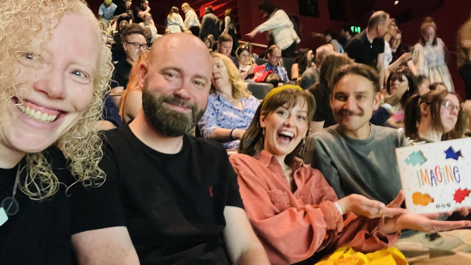 Members of the RY team in the audience of the Birmingham Design Festival, smiling and holding a programme that reads 'Imagine'
