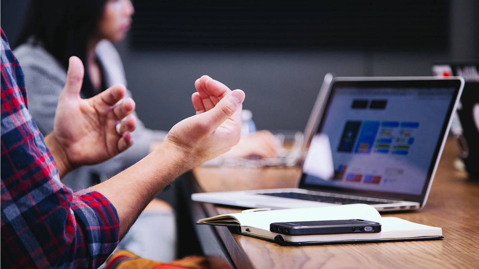 Hands gesturing in front of a notepad and computer in an office setting