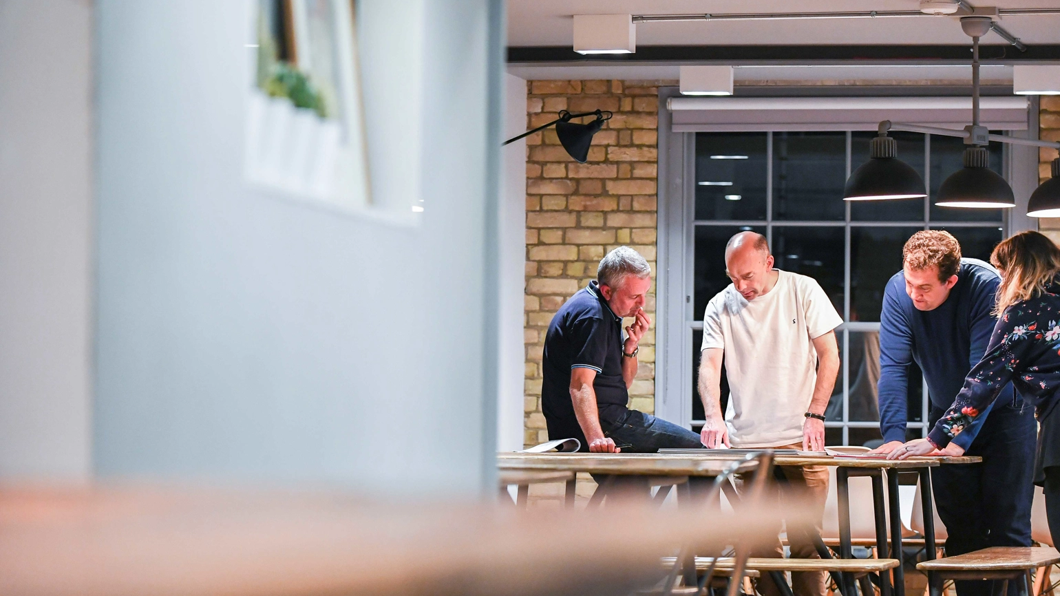 A team of four people gathered around a table, all looking down at it