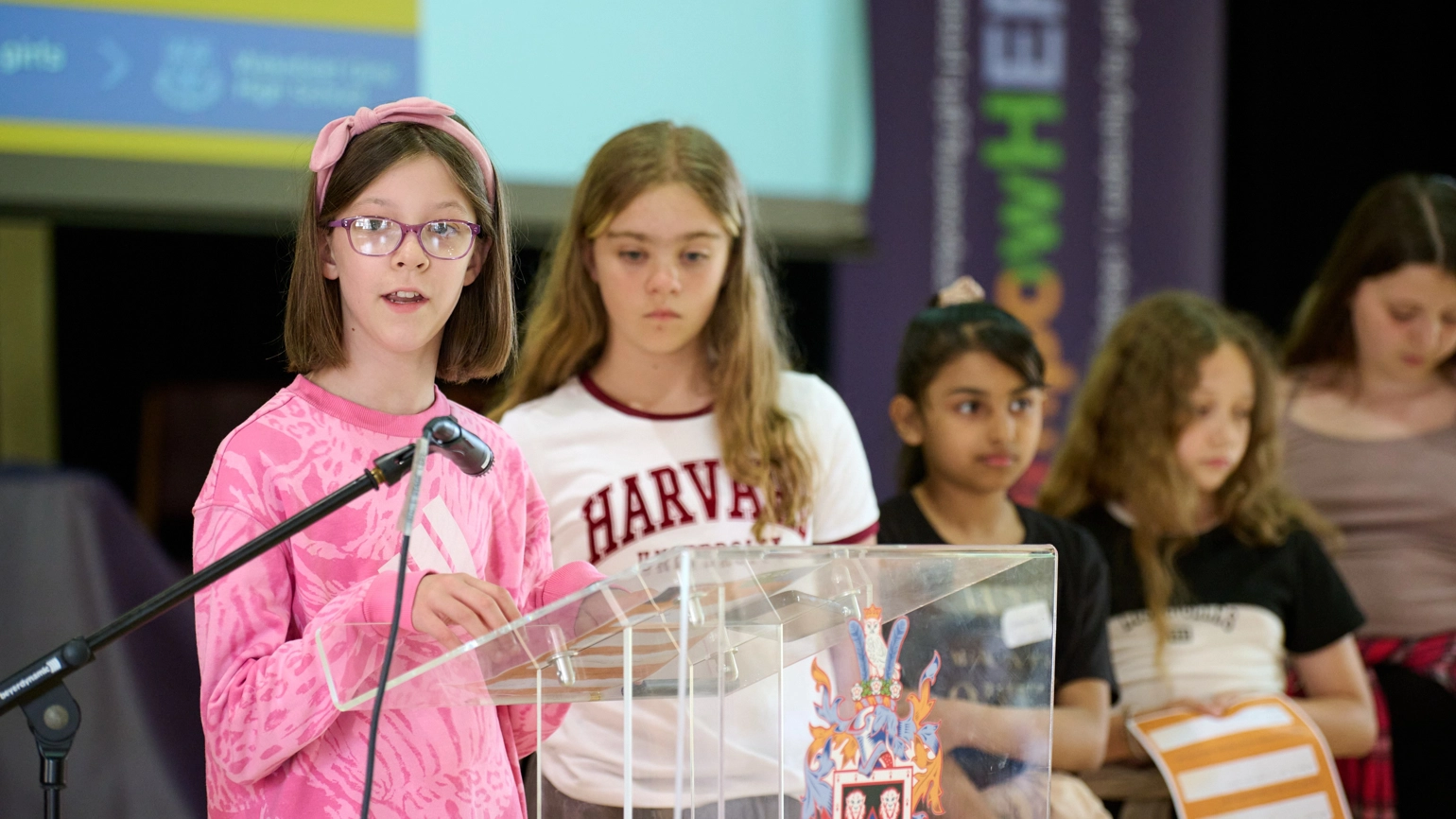 A group of young girls talking in front of a podium at EmpowerHer event