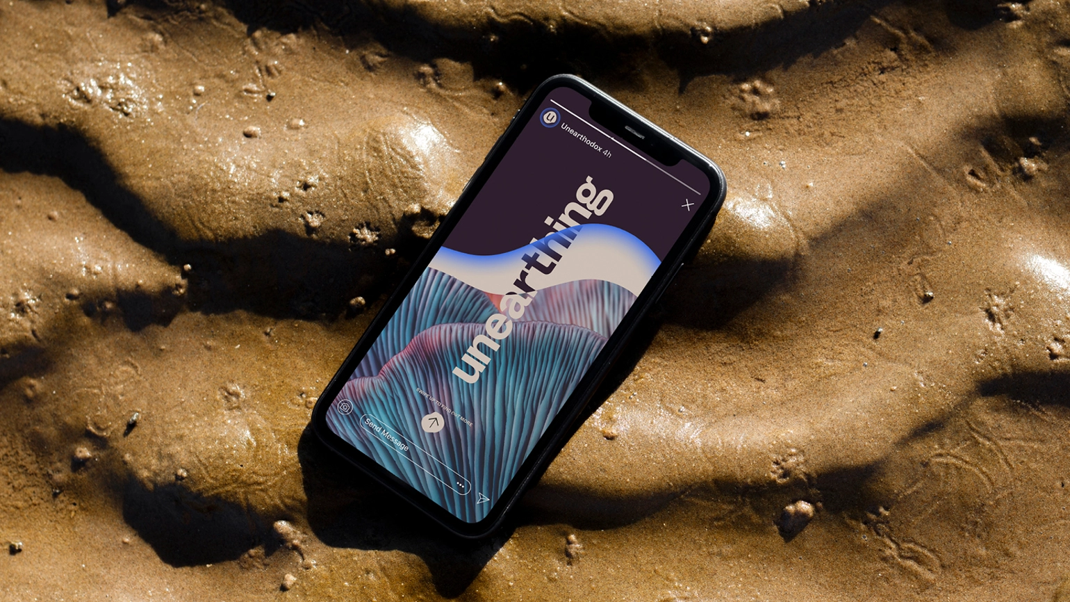 A phone sitting sideways in waves of earthy sand, the screen shows the word 'unearthing'