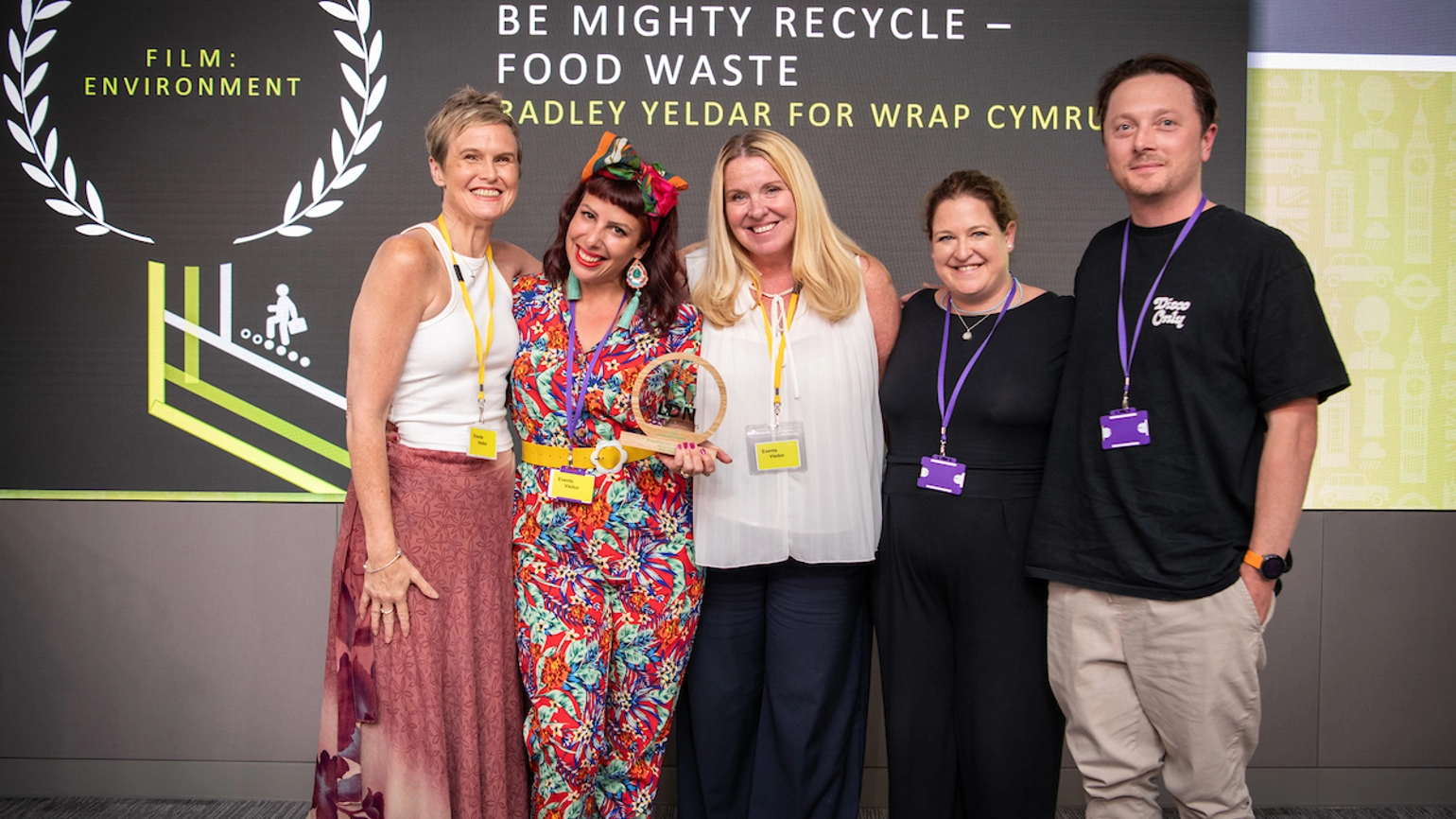 RY team members and their clients in front of an Evcom Clarion Awards 2023 background, holding a round glass and wood trophy